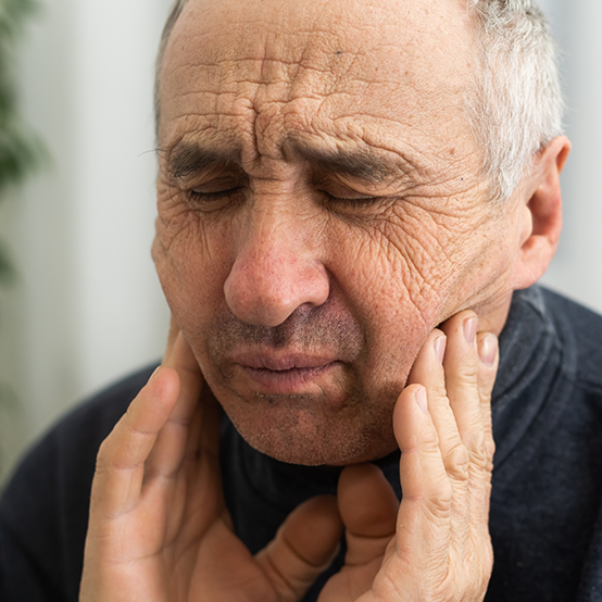 Senior man wincing and holding the sides of his jaw in pain