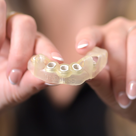 Hands holding a clear plastic guide for surgical dental implant placement